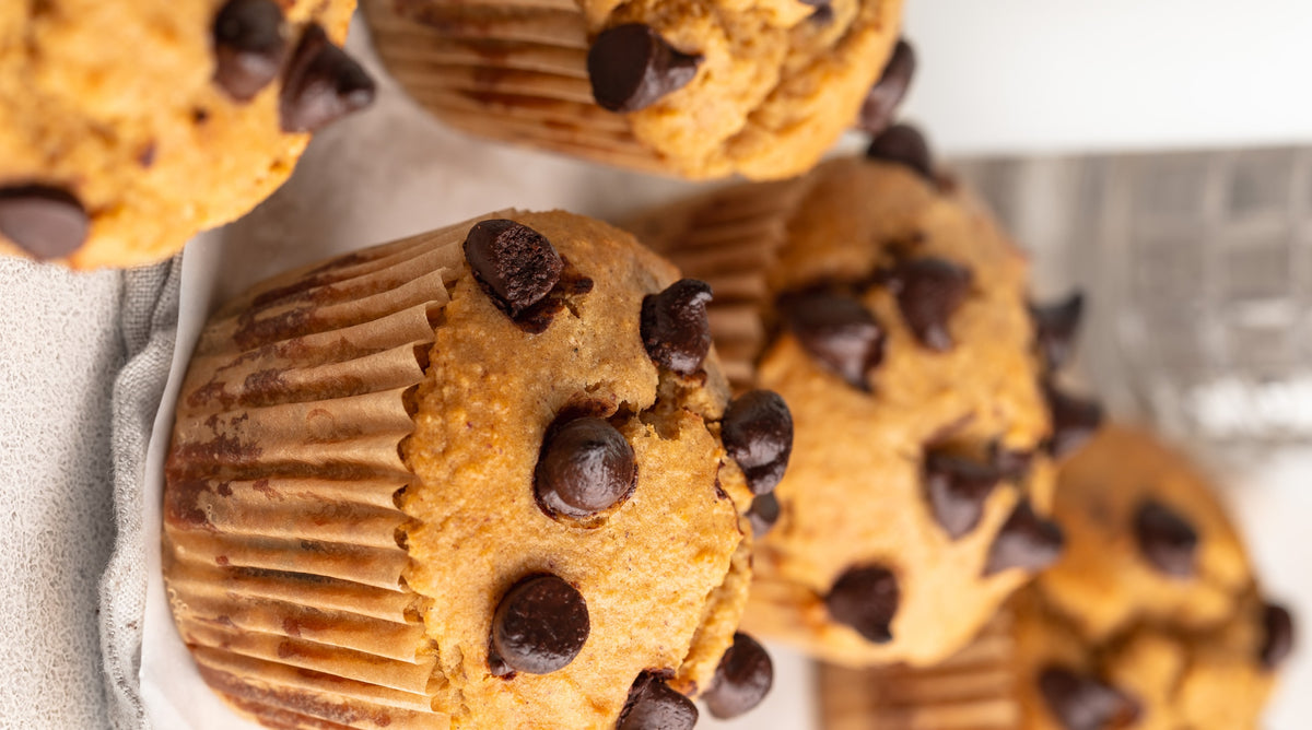 Close-up of several chocolate chip muffins in paper liners, with one muffin in sharp focus in the foreground and more softly blurred in the background.