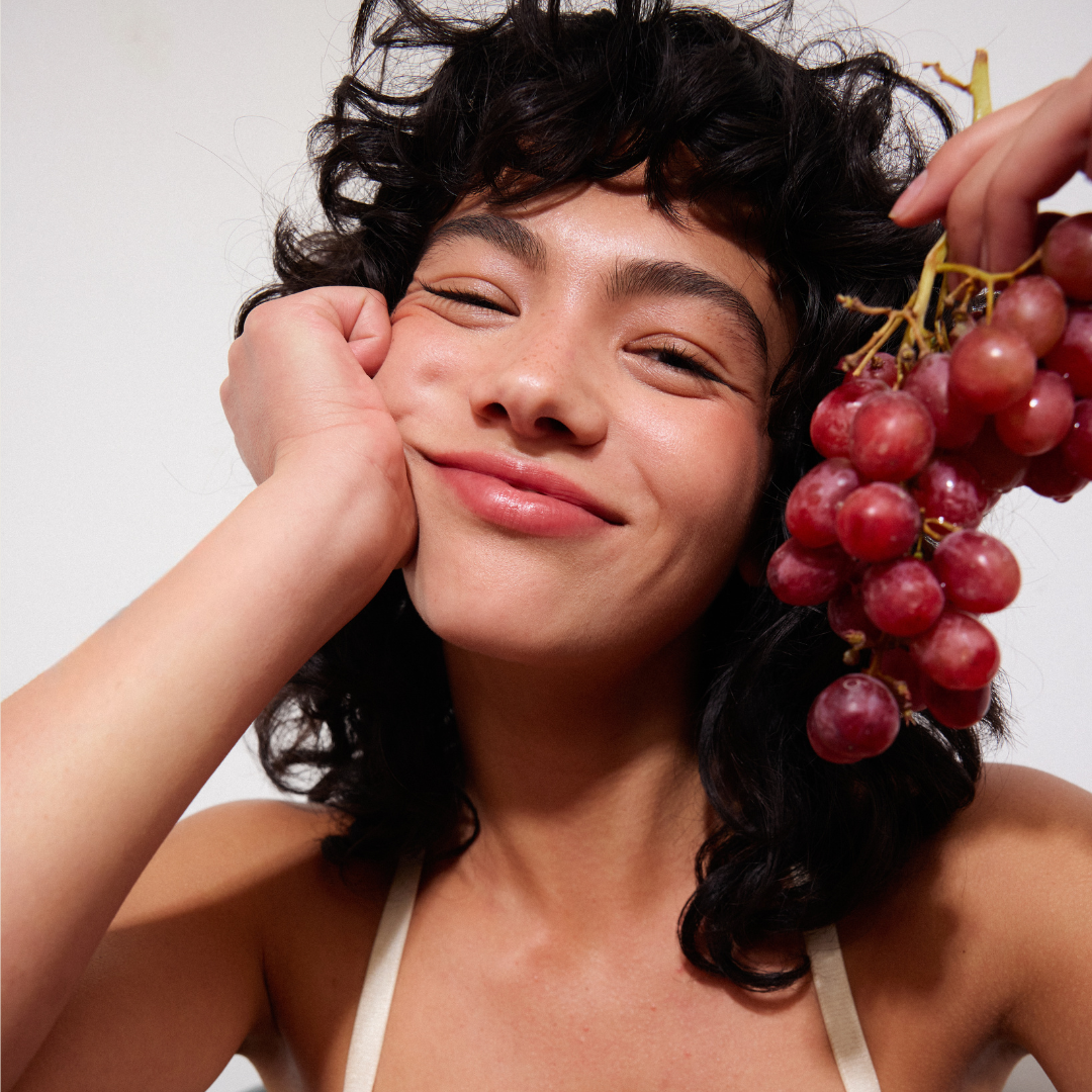 Woman holding a bunch of grapes with a neutral background