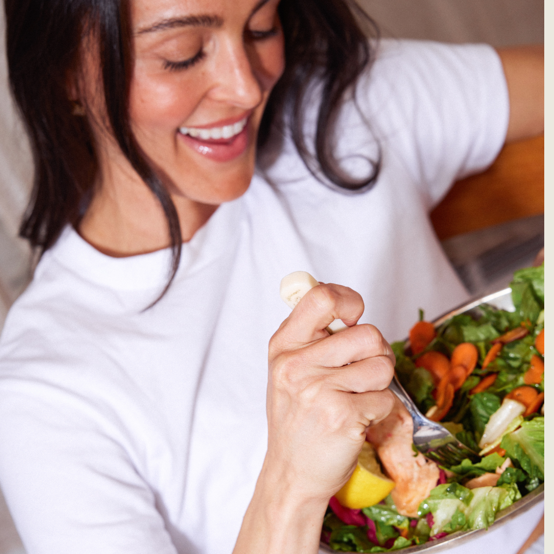 Megan eating a salad with a fork, wearing a white shirt.