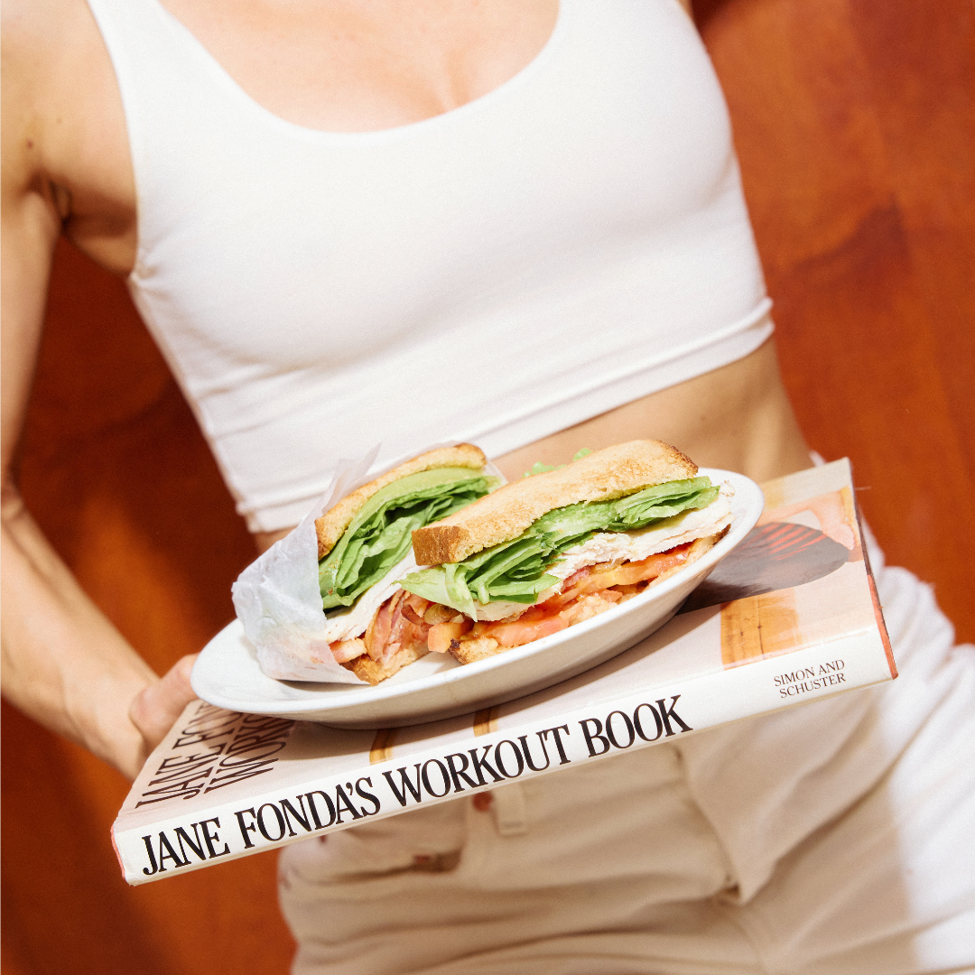 Person holding a sandwich on a plate over a book titled 'Jane Fonda's Workout Book'.