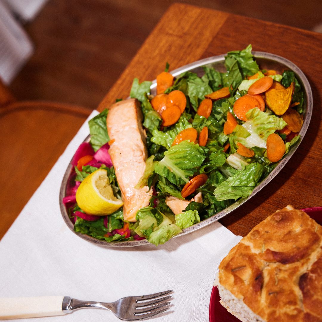 Salad with salmon, carrots, and lettuce on a wooden table with bread and lemon.