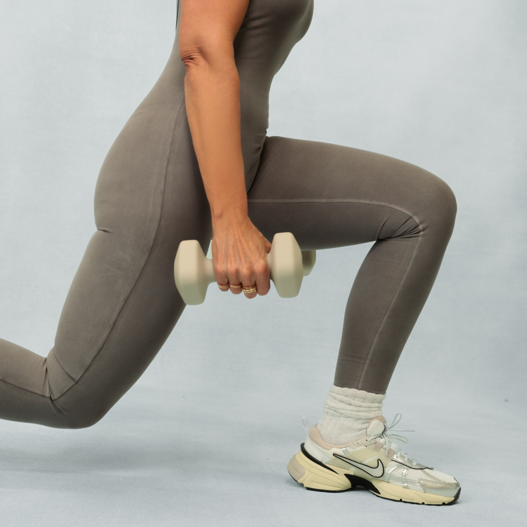 Person performing a lunge exercise with a dumbbell on a plain background