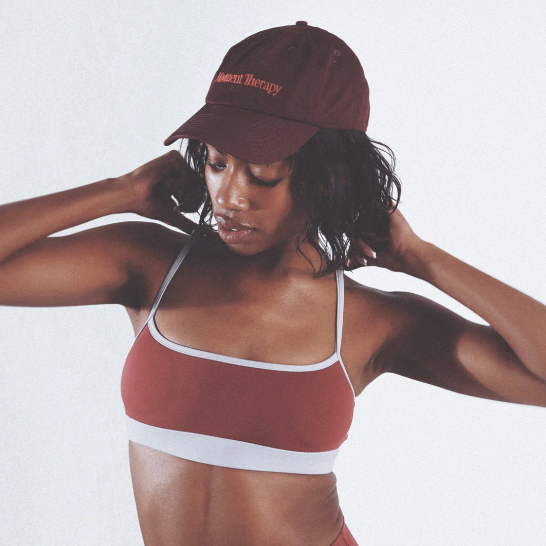 Woman wearing a burgundy sports bra and cap on a light background