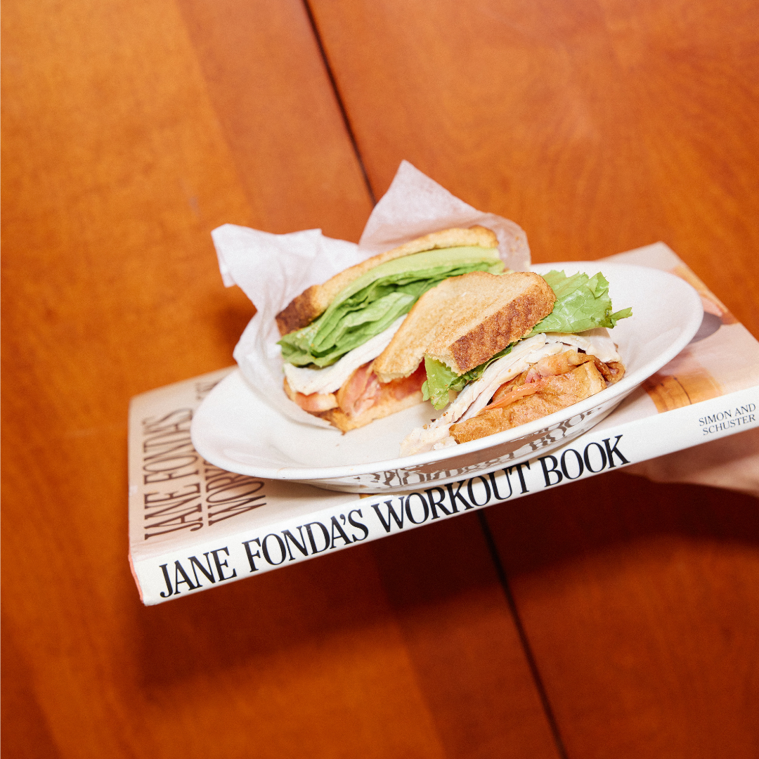 Sandwich on a plate over Jane Fonda's Workout Book against a wooden surface