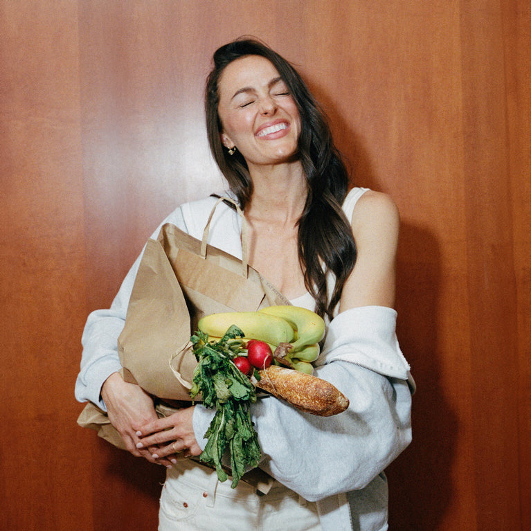Megan holding groceries against a wooden wall