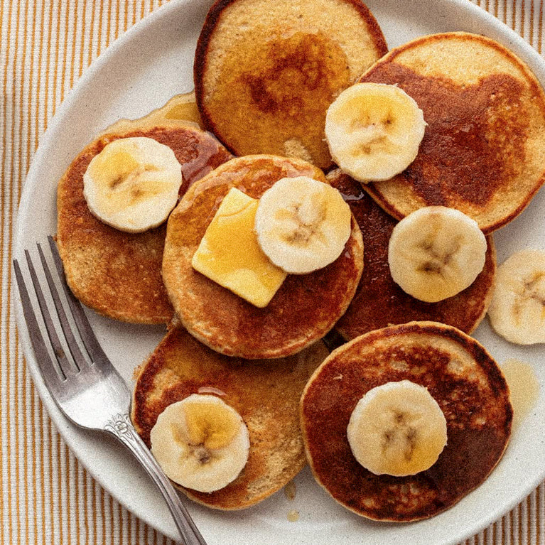 Pancakes with banana slices and syrup on a white plate with a fork.