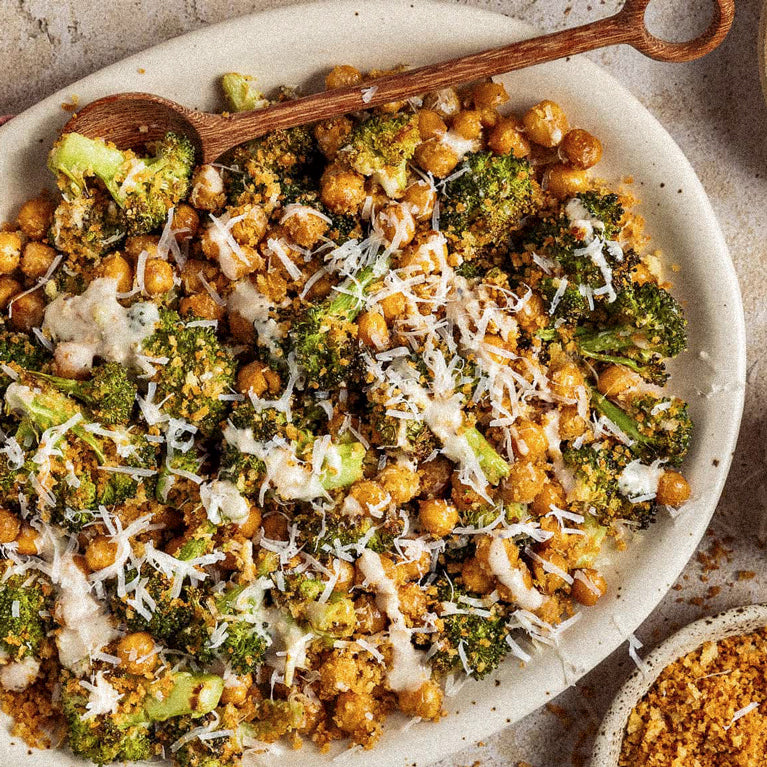 Plated dish of roasted broccoli and chickpeas with parmesan cheese on a stone surface.