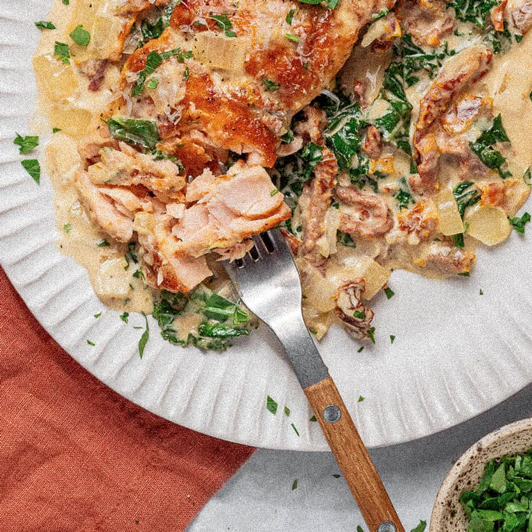 Plated dish of creamy salmon and vegetables with a fork on a white plate.