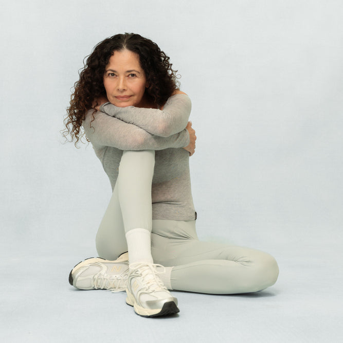 Woman in light gray outfit sitting on a white background
