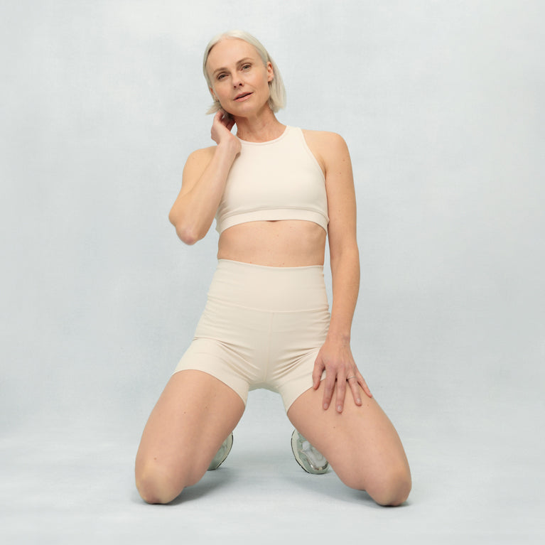 Woman wearing a beige sports bra and shorts on a light gray background