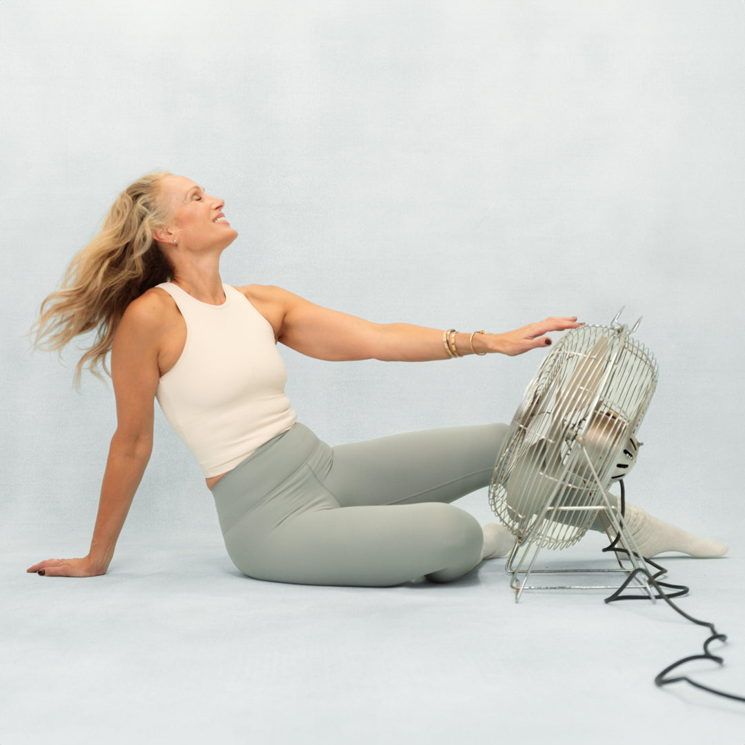 Woman sitting on the floor with a fan to her side against a plain background